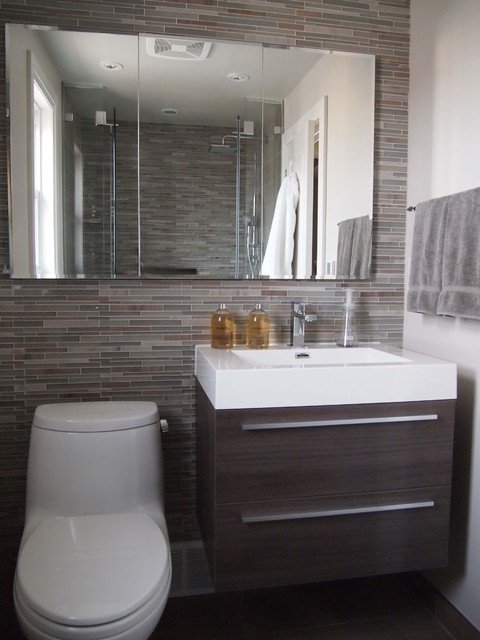 Wall on which a washbasin with wooden cabinet, toilet and large mirror is installed.  Tiles in different shades of brown and gray