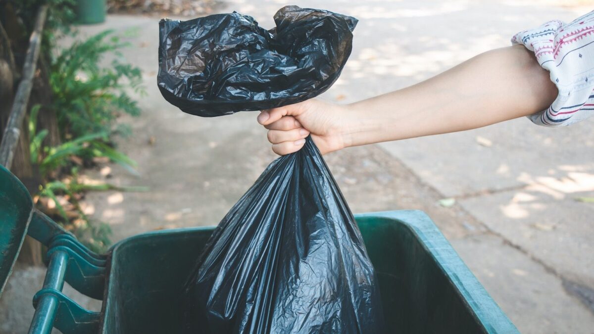 Cropped Hand Of Woman Putting Plastic Bag In Dustbin